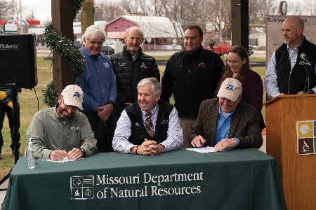 Governor Mike Parson, center, watches as MoDNR director Dru Buntin, left, and Mark Birk of Ameren Missouri sign an agreement to transfer ownership of the Rock Island corridor to the state of Missouri.