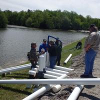 A series of siphons are assembled to safely lower the level of a lake in order to reduce risk while repairs are made.