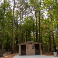 The overlook at the bottom of the Interpretive Loop Trail at Grand Gulf State Park is one of four that were recently replaced. Alt. text: Nestled below pine and oak trees is a small bathroom building with two doors, one marked men and the other women. There is a metal trash can in the bottom right of the image.