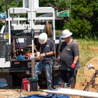 Well drilling contractors complete construction of a new well as they install pipe and wire electrical lines to the pump.