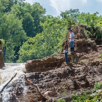 Water rushes from a partial breach in the Glover Spring Lake Dam in Fulton, on Aug. 3, 2016, as department staff assess the damage. The department assisted Callaway County officials in evaluating the risks associated with the breach and advised landowners on repair.