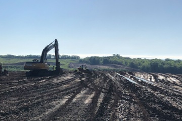 A backhoe sits in a muddy field filled with tire tracks from earth-moving equipment.