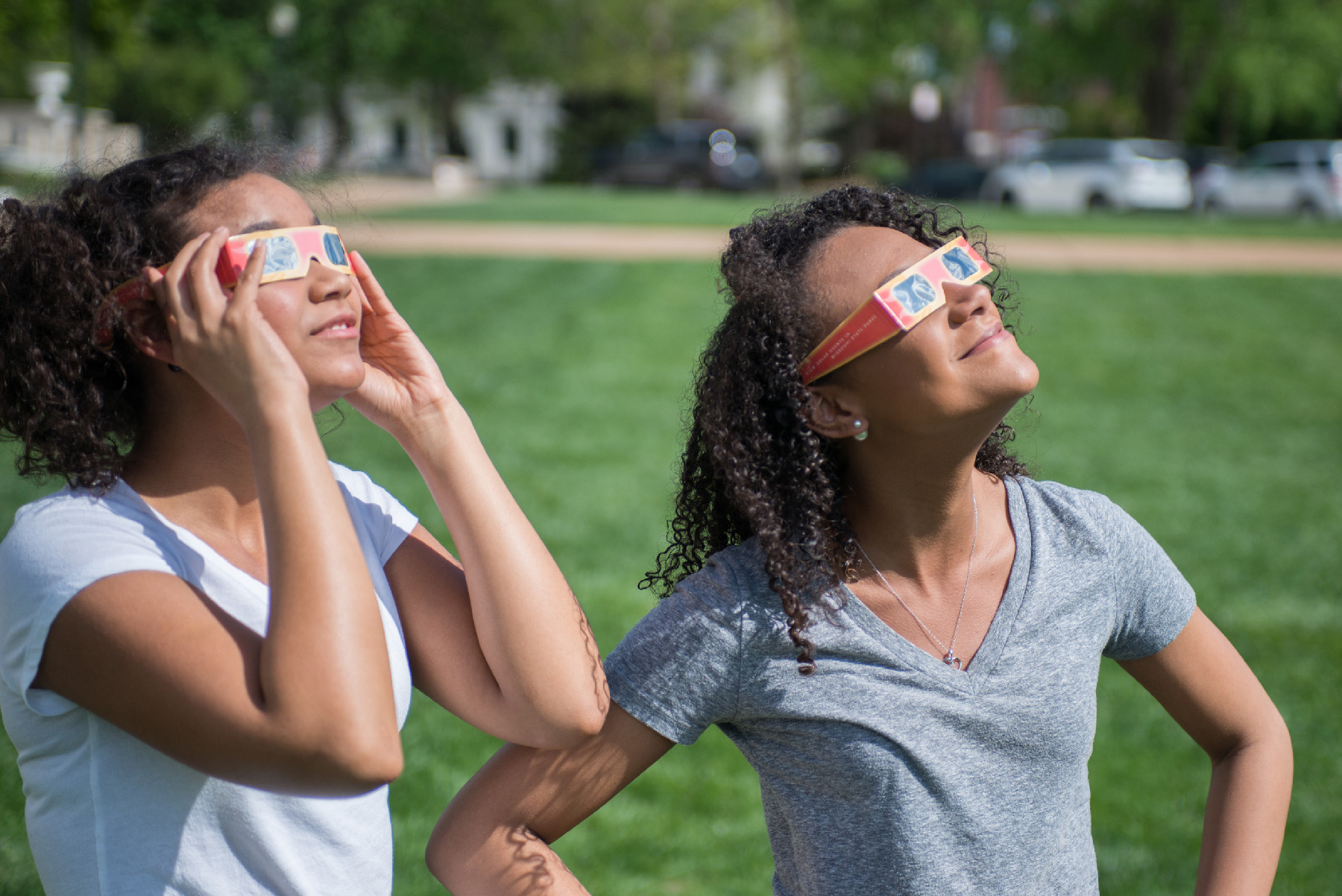 Two women look up at the sun. They are wearing eclipse glasses.