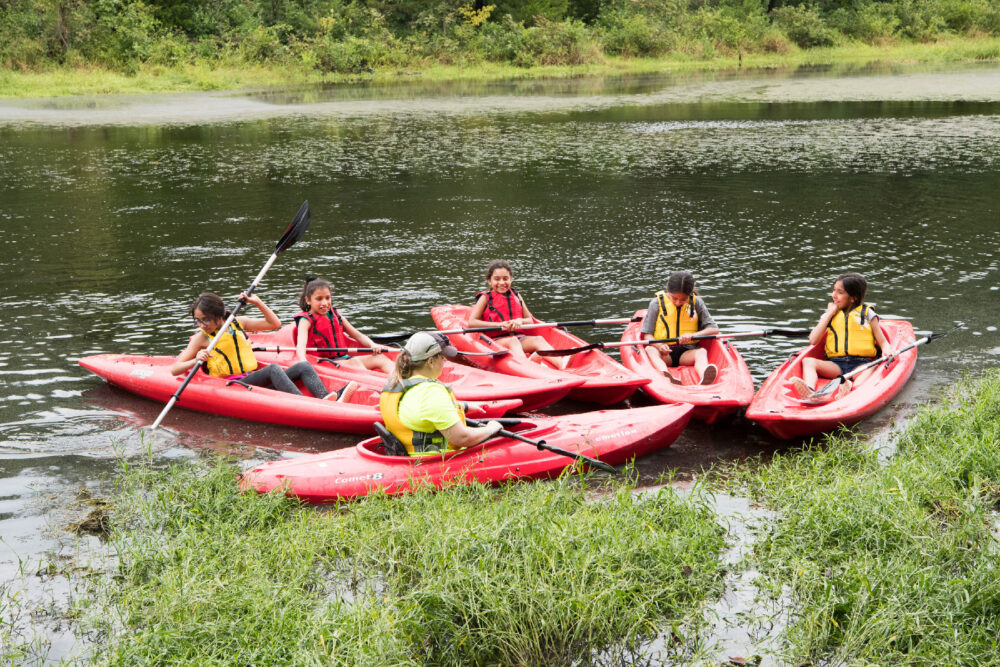 A group of five children and one instructor float as a group in kayaks.