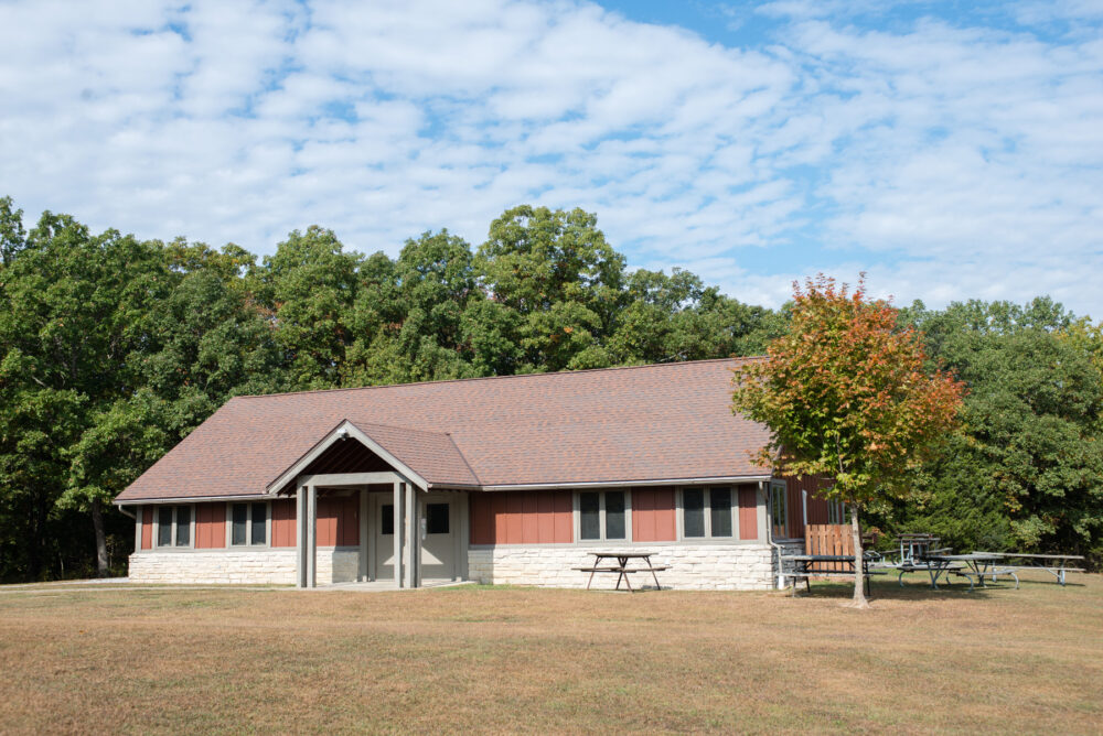 A stone and wood banquet hall building. Picnic tables are on the left side of the building.