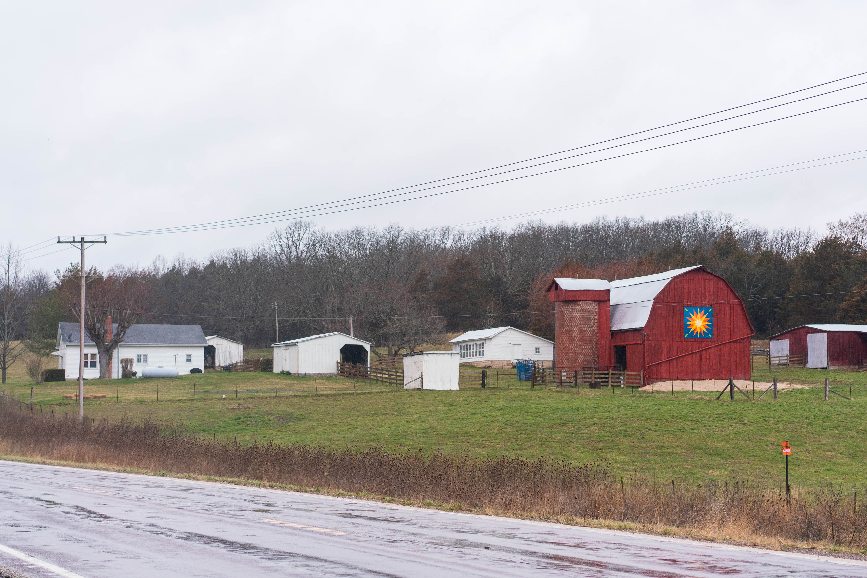 A wide view of a farm. A large barn is on the right, with several outbuildings in the middle and a farmhouse on the left.