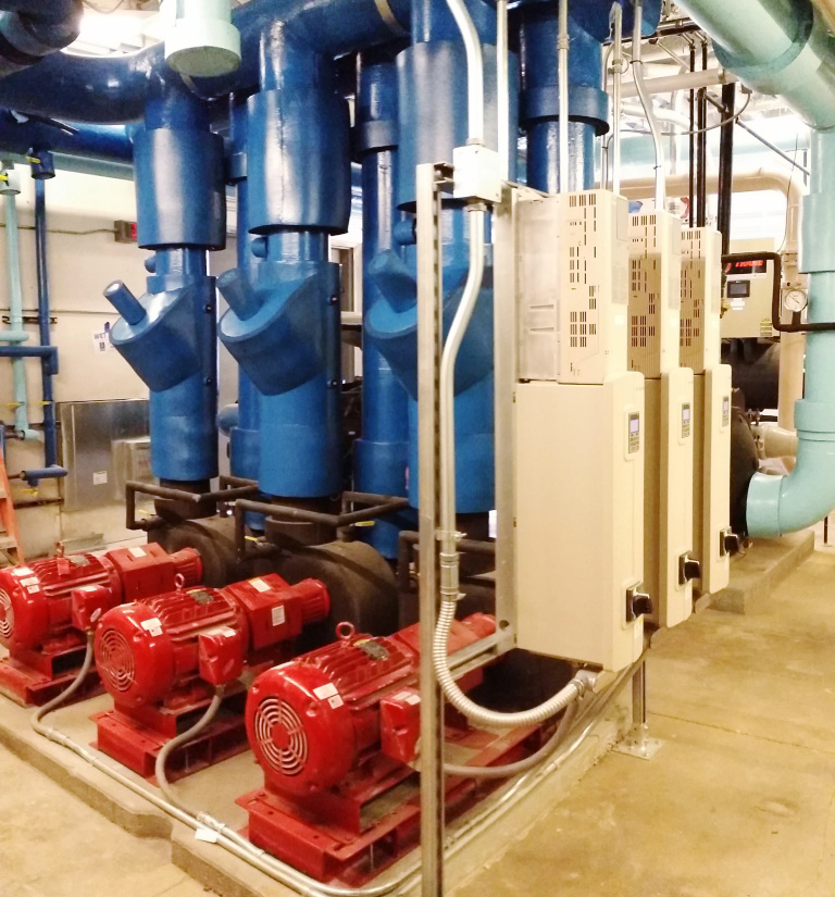 Large metal pipes wrapped in insulation. At the base of the pipes is a motor. Part of an HVAC. The pipes are located in a mechanical/machinery room at a hospital building.