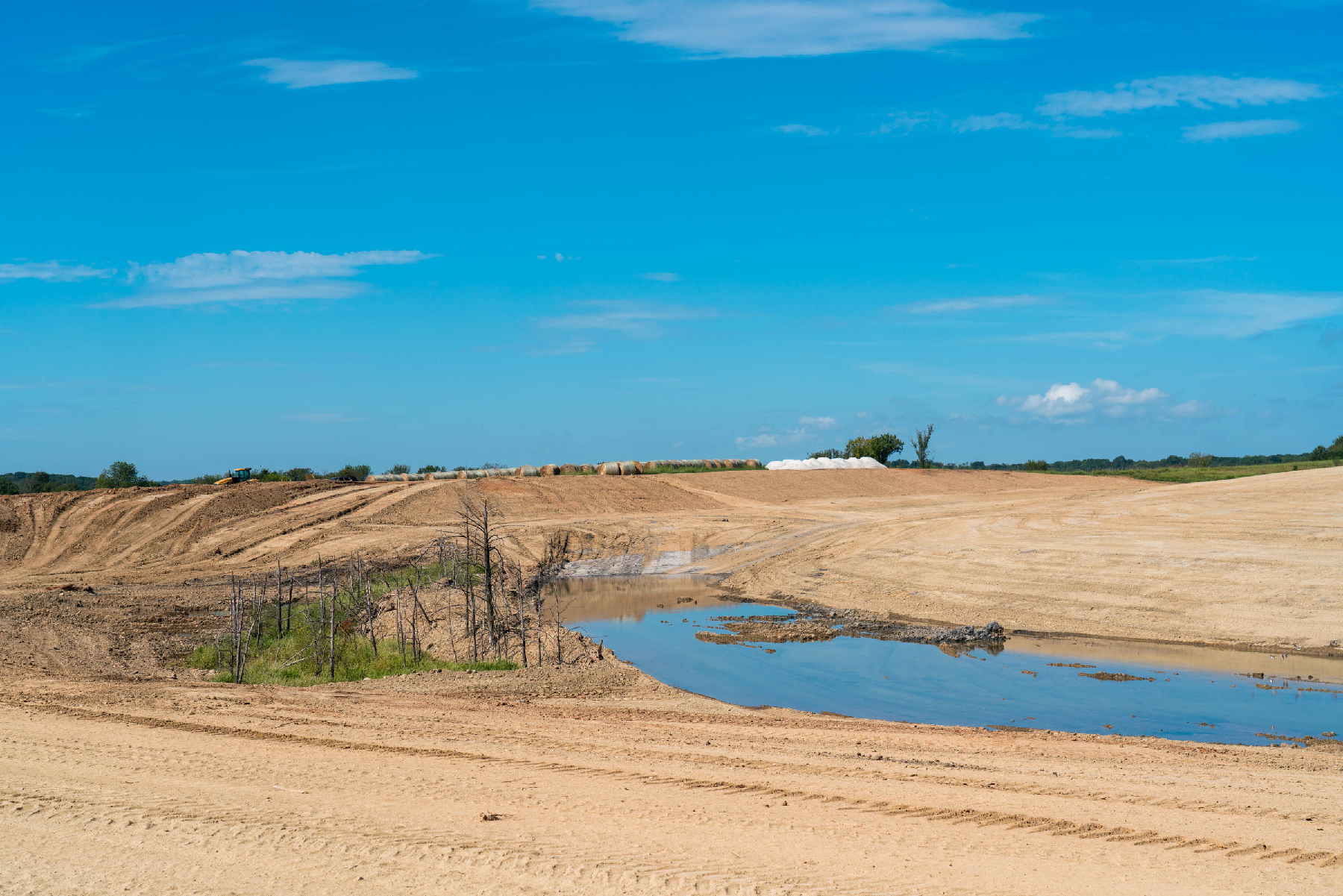 A wide view of a field that has been stripped of all vegetation. The ground is covered with fresh fill dirt. A low spot holds water.