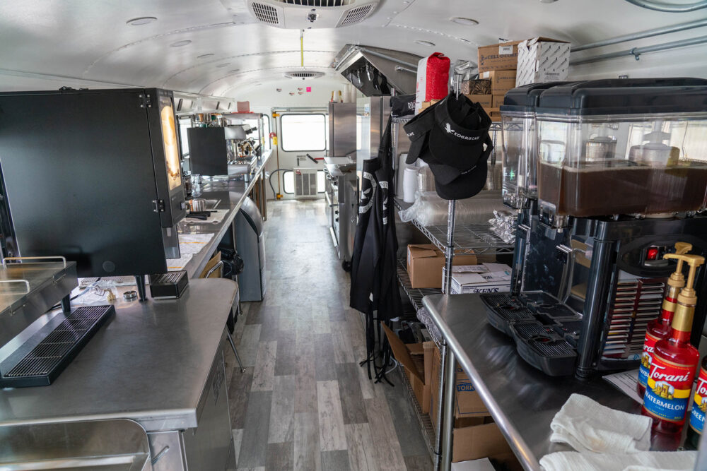 The interior of a bus, except the seats have been removed and replaced with stainless steel counter tops for food preparation, related appliances and shelving for storage.