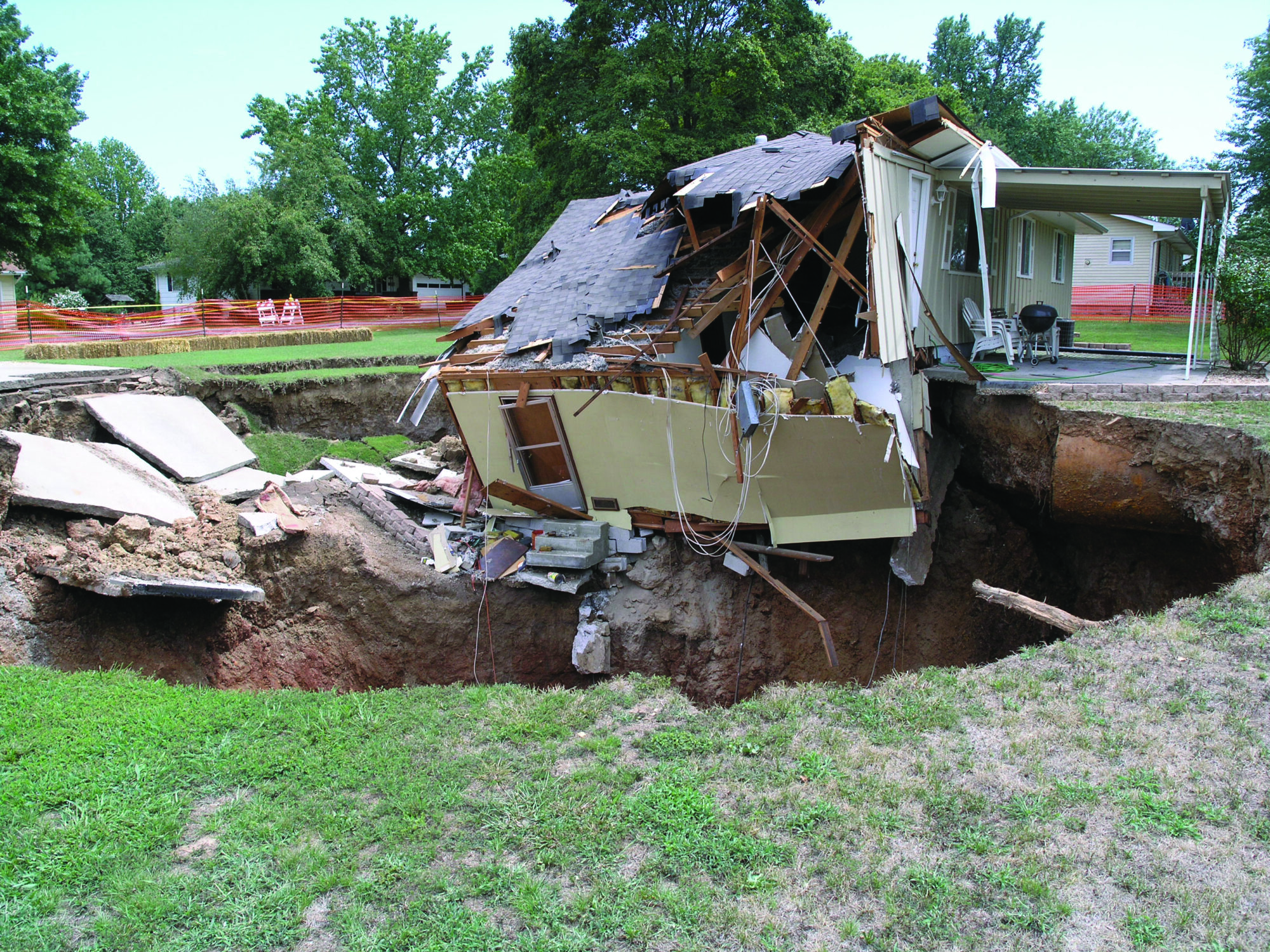 Photo of a home partially collapsed into an open sinkhole.