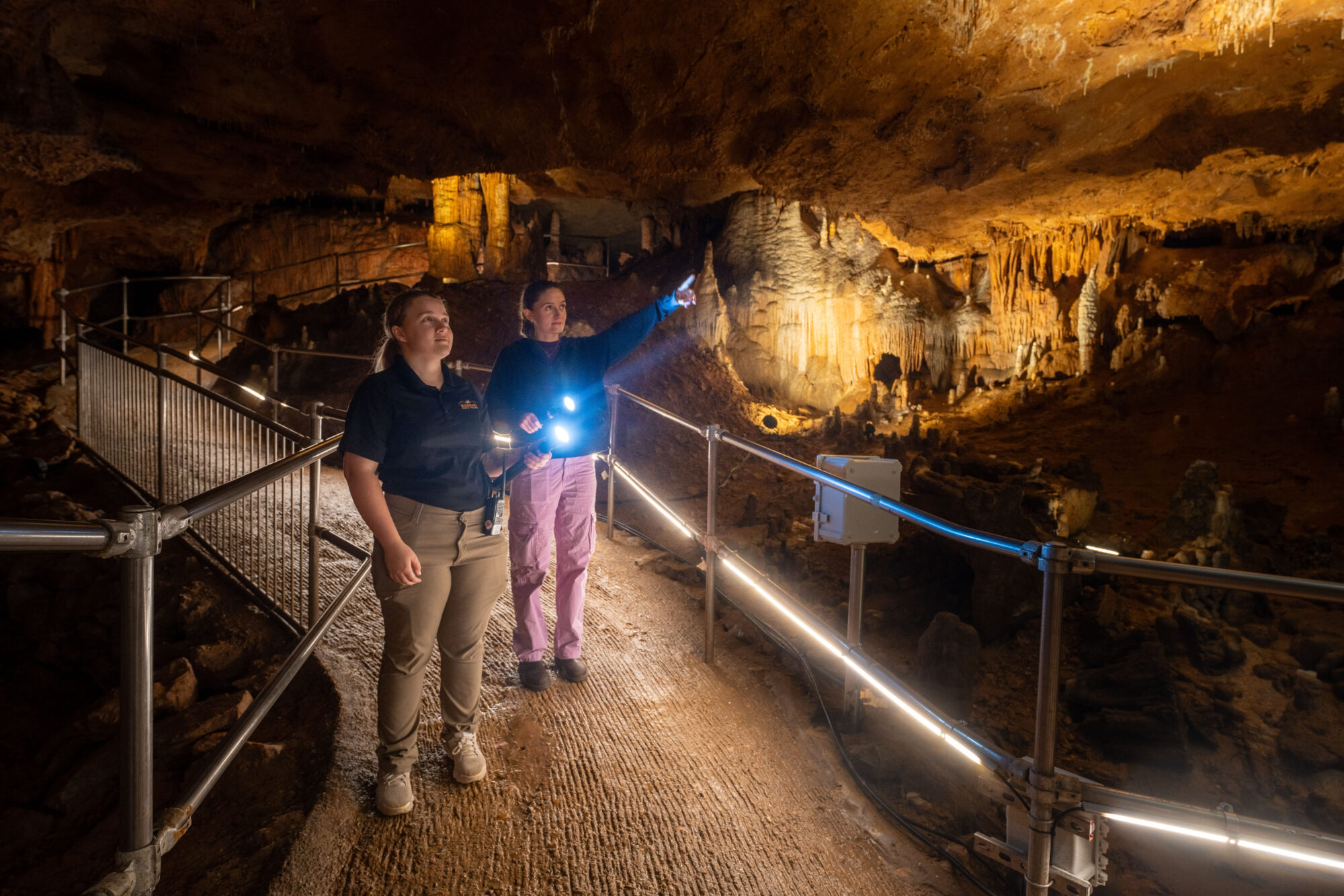 Photo of two people in a cave, one pointing in a direction while in conversation.