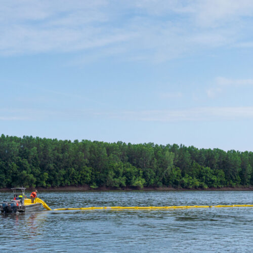 Photo of people in a boat placing containment booms into a river.