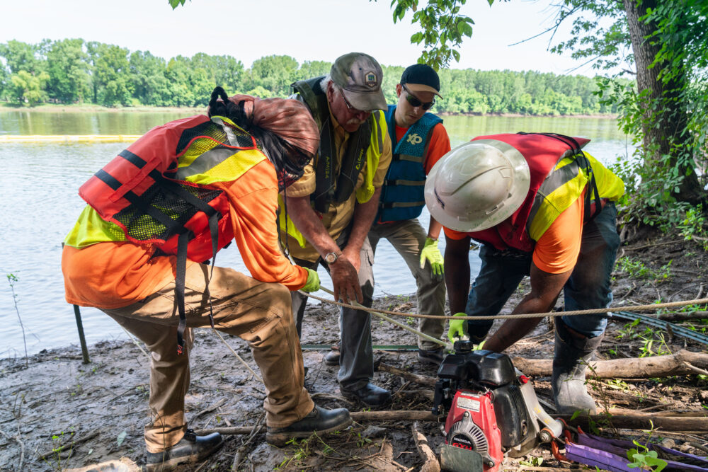 Photo of people gathered around fixing equipment on a shoreline.