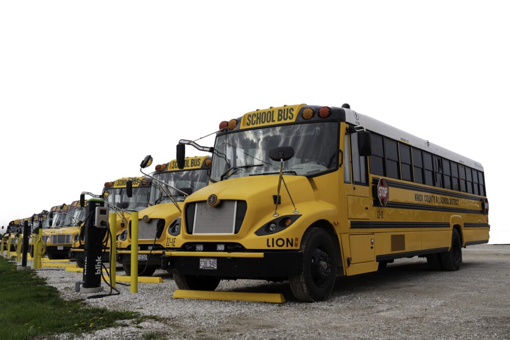 Photo of electric school buses lined up at charging stations.