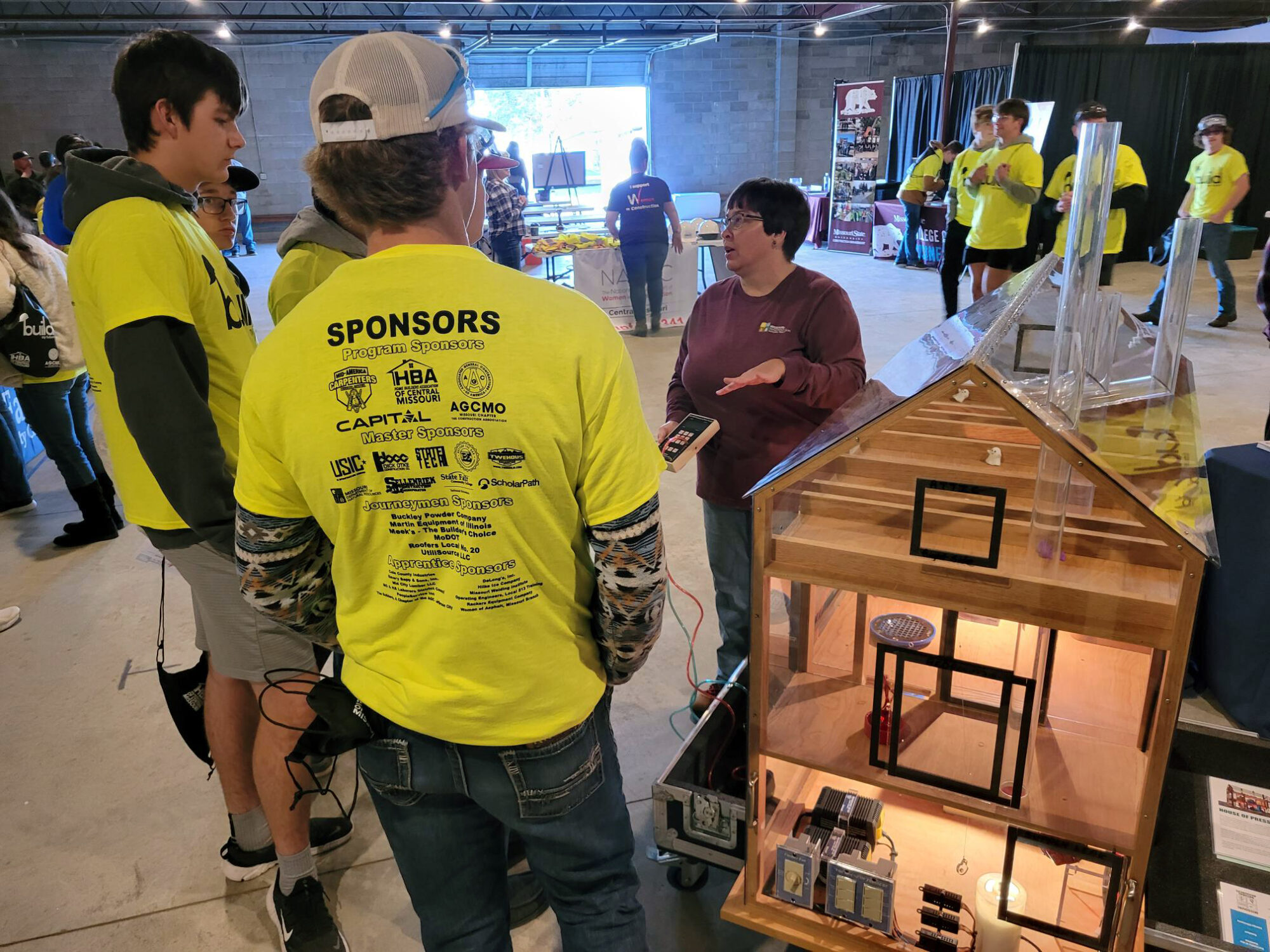 Photo of people talking next to a diorama of a home.