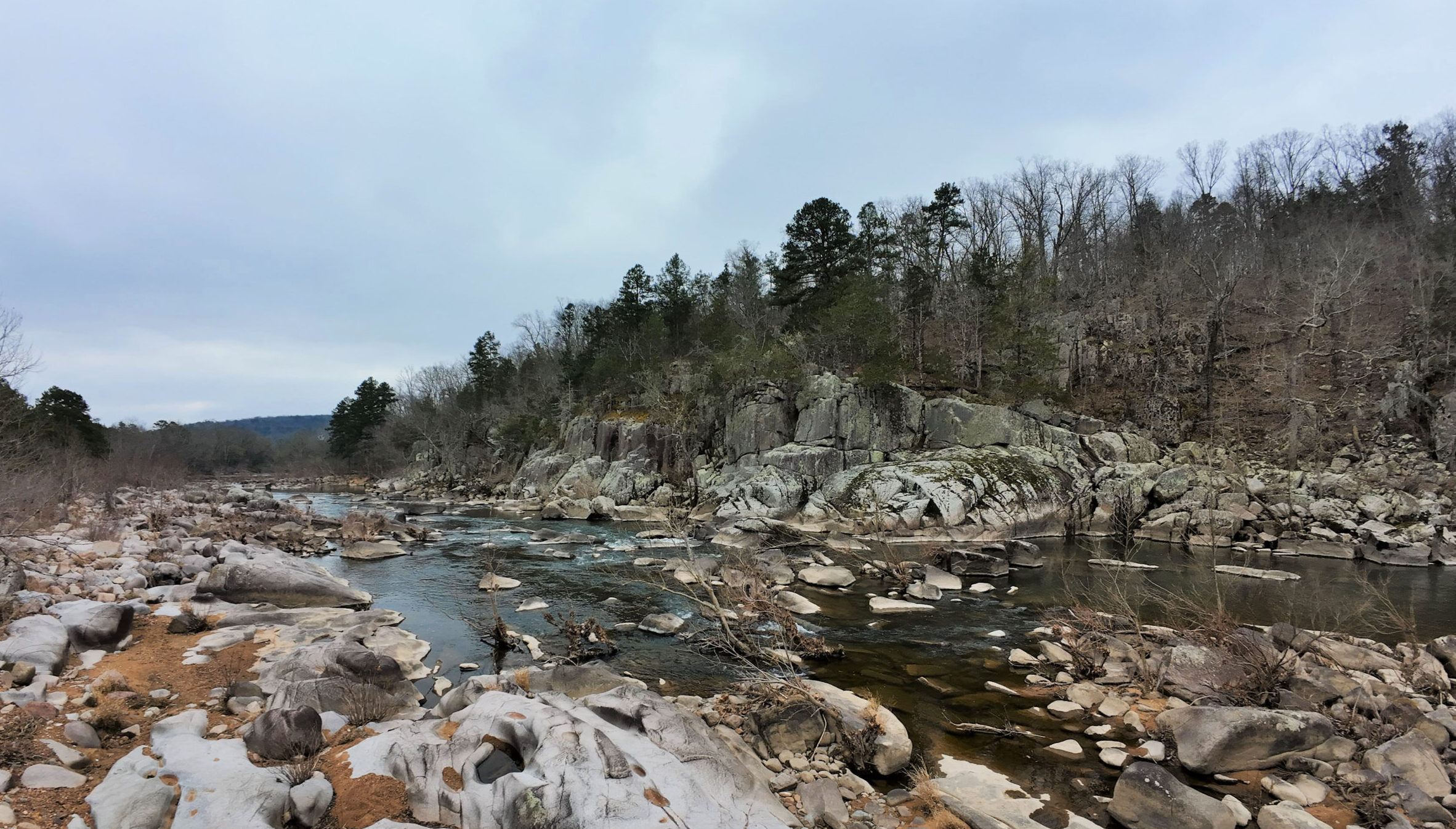 Photo of a river flowing through rocks of various sizes surrounded by trees.