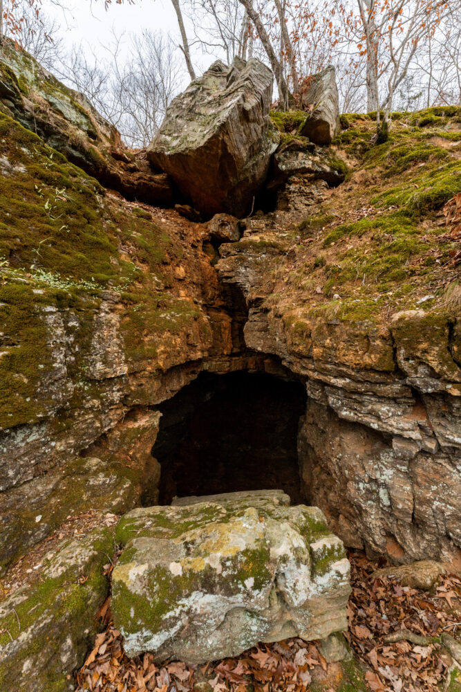 Photo of a large bolder in front of a cave opening.