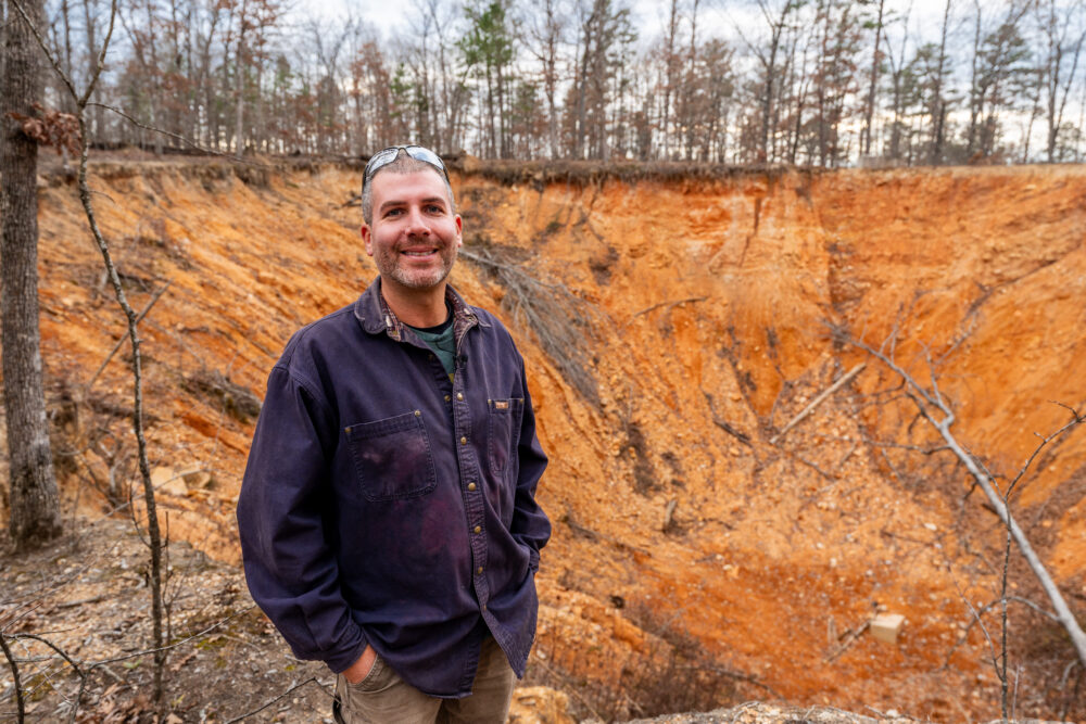 Photo of a man in front of a sinkhole.