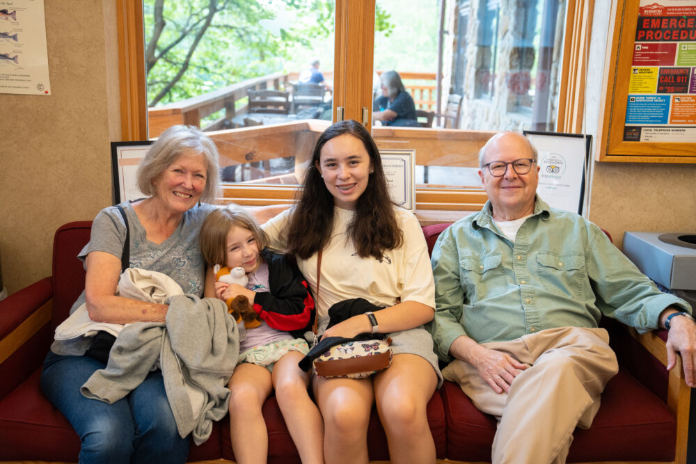 Photo of a group of people, various ages, sitting on a couch facing the photographer.