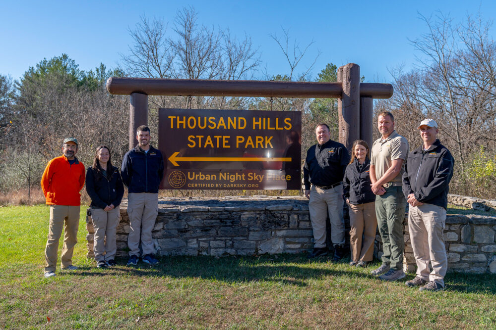 A group of people standing either side of a state park sign.