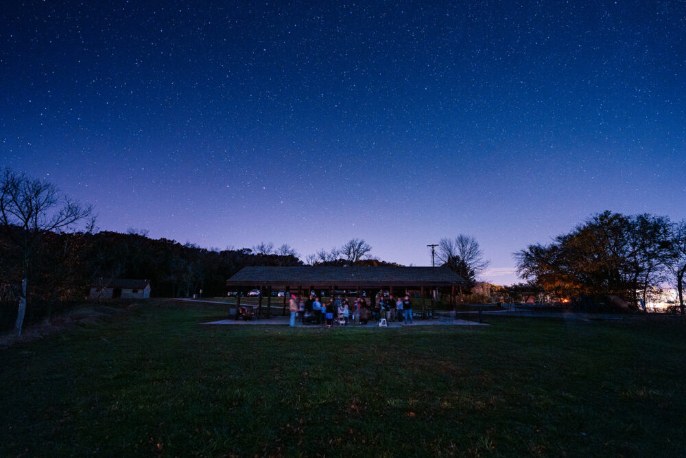 A pavilion with people gathered below, a star filled sky above.
