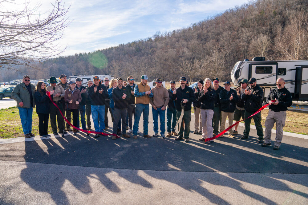 People lined up facing the camera with a ribbon cut in half fluttering to the ground.