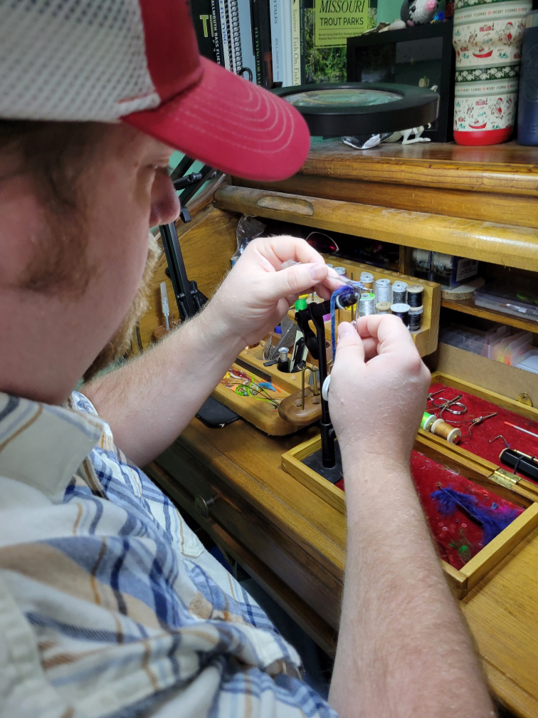 Man at a work station wrapping a fishhook to create a "fly"