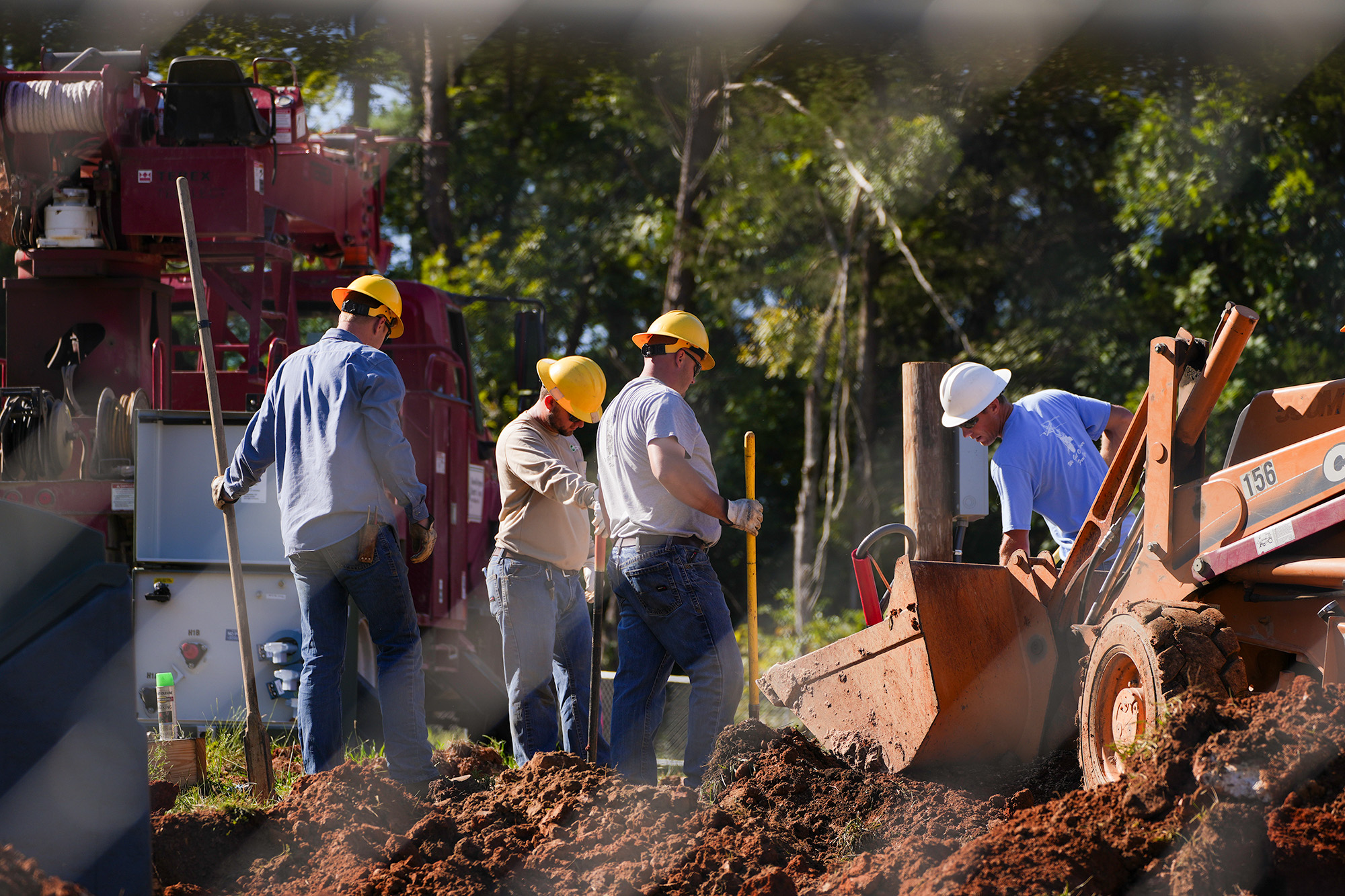 Construction workers gathered around a large back-hoe digging a hole.