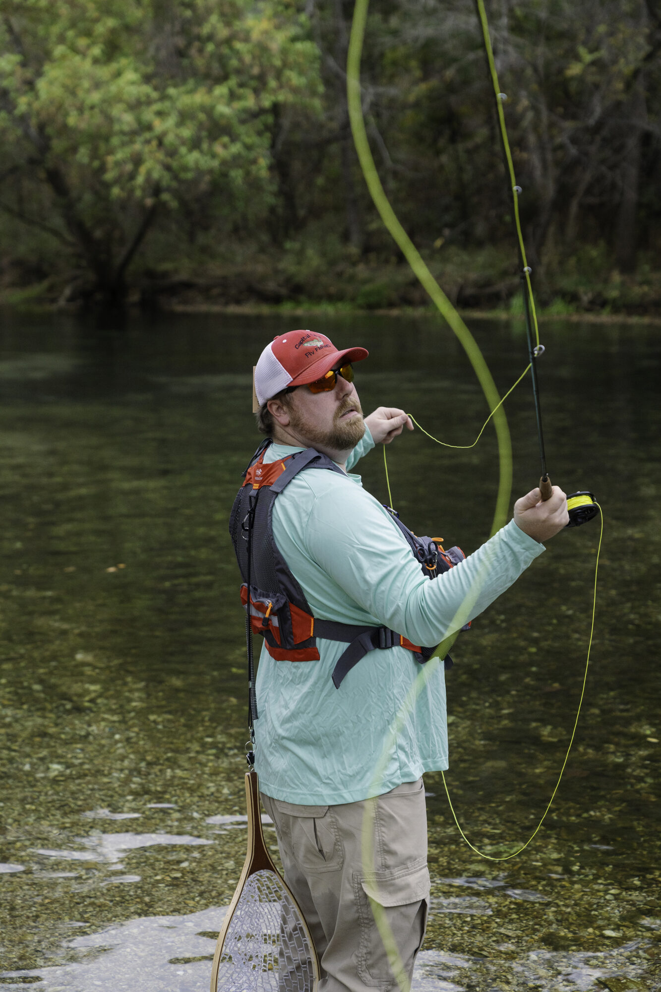 Man stands in a river looking back over his shoulder as he throws a fly fishing line back and forth to begin fishing.