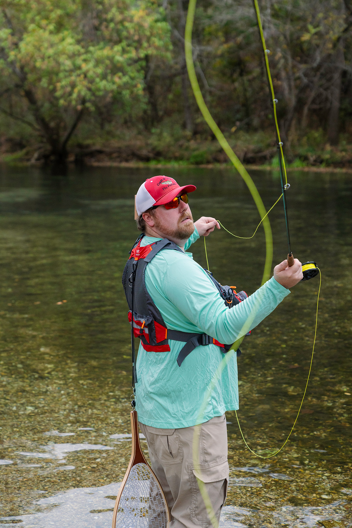 Man stands in a river looking back over his shoulder as he throws a fly fishing line back and forth to begin fishing.