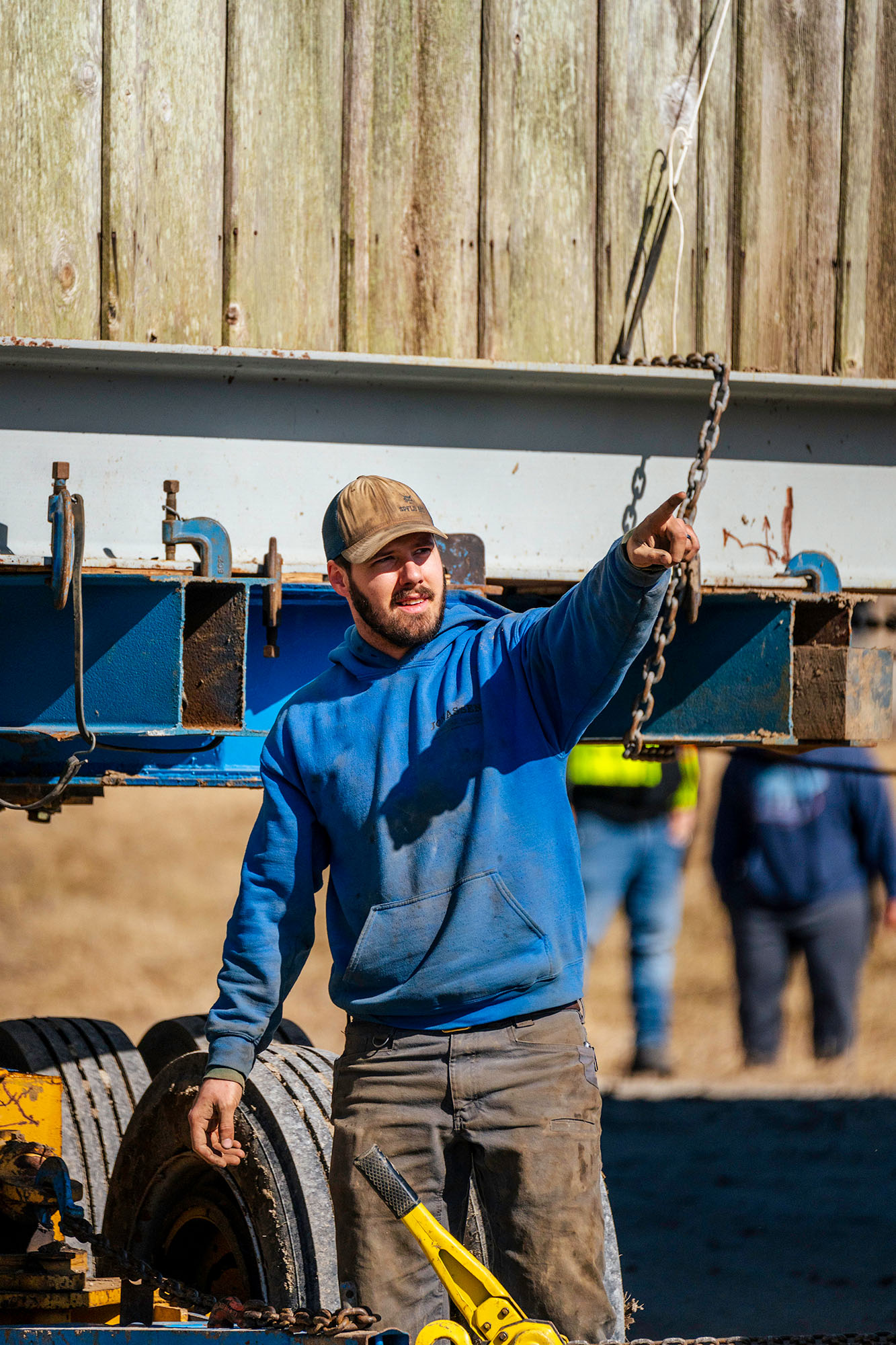 Man next to large steel beams holding a portion of a wooden structure. He is pointing his finger to direct others who are standing outside of the photograph frame.