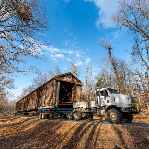 Large covered bridge is towed down a road by a single cab semi-truck.