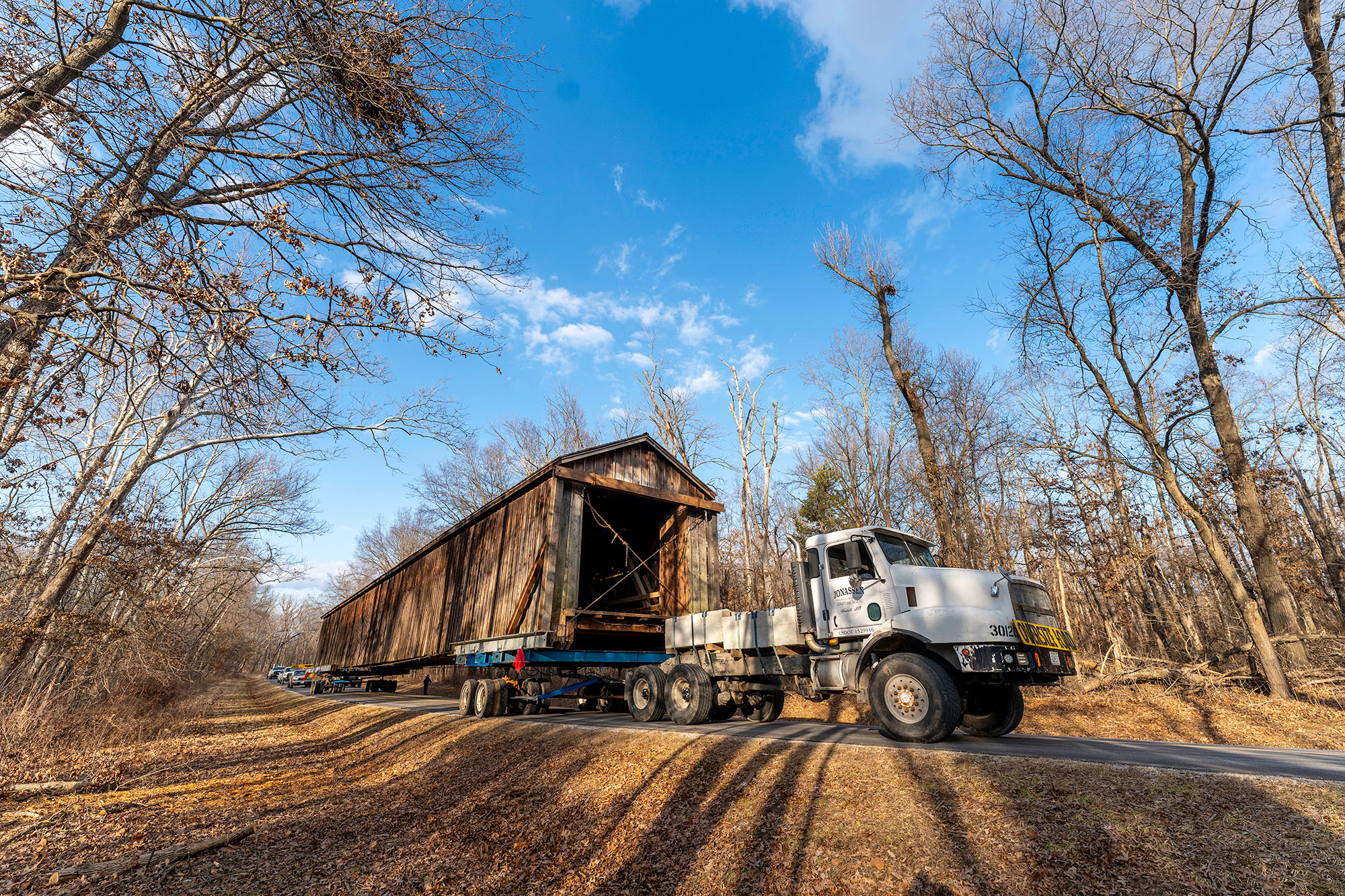 Large covered bridge is towed down a road by a single cab semi-truck.