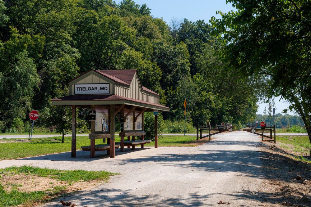 Small shelter pavilion with benches and information placards sits next to a gravel trail.