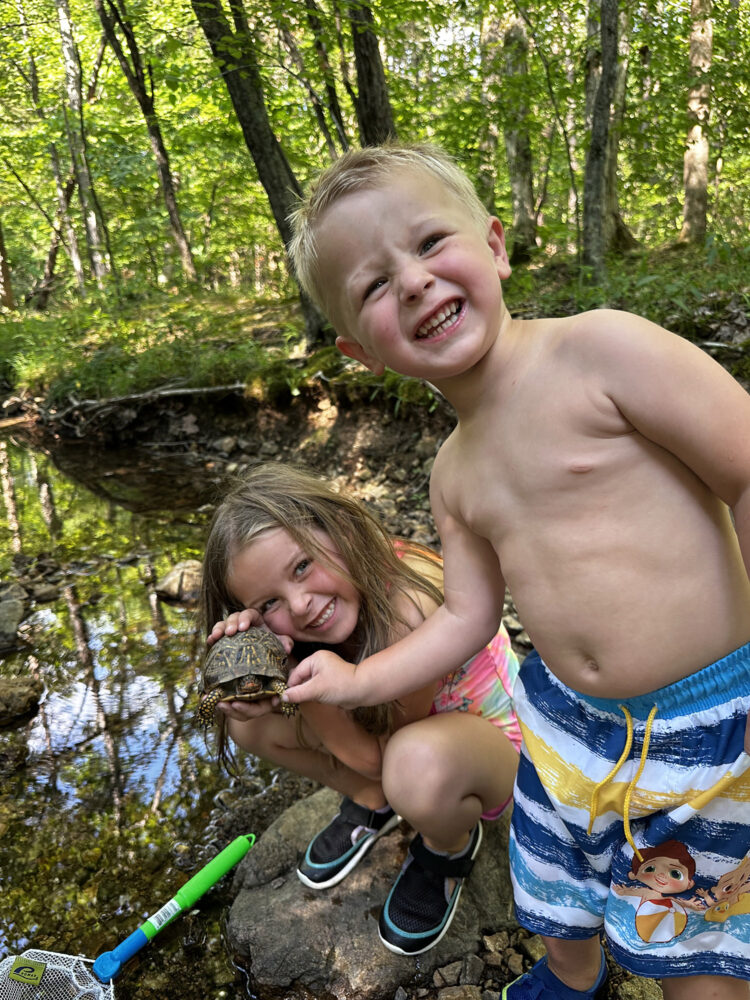 Two children pose next to a creek with a box turtle.