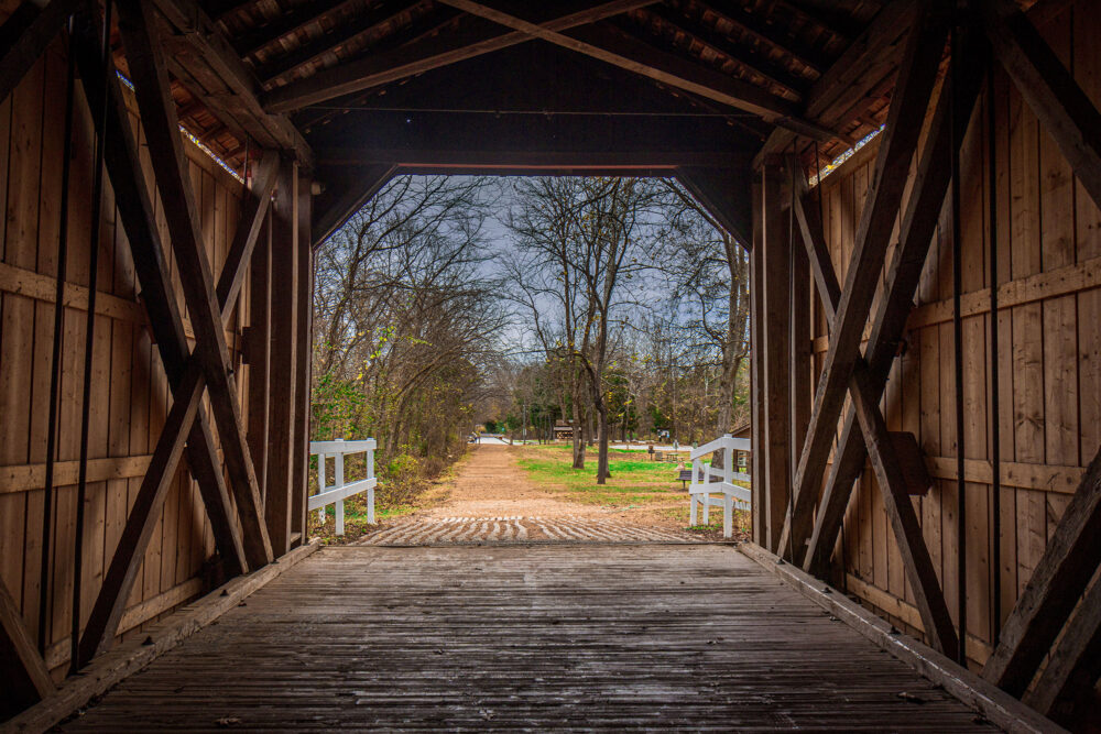 A view of a gravel path framed by the opening of a wooden covered bridge.