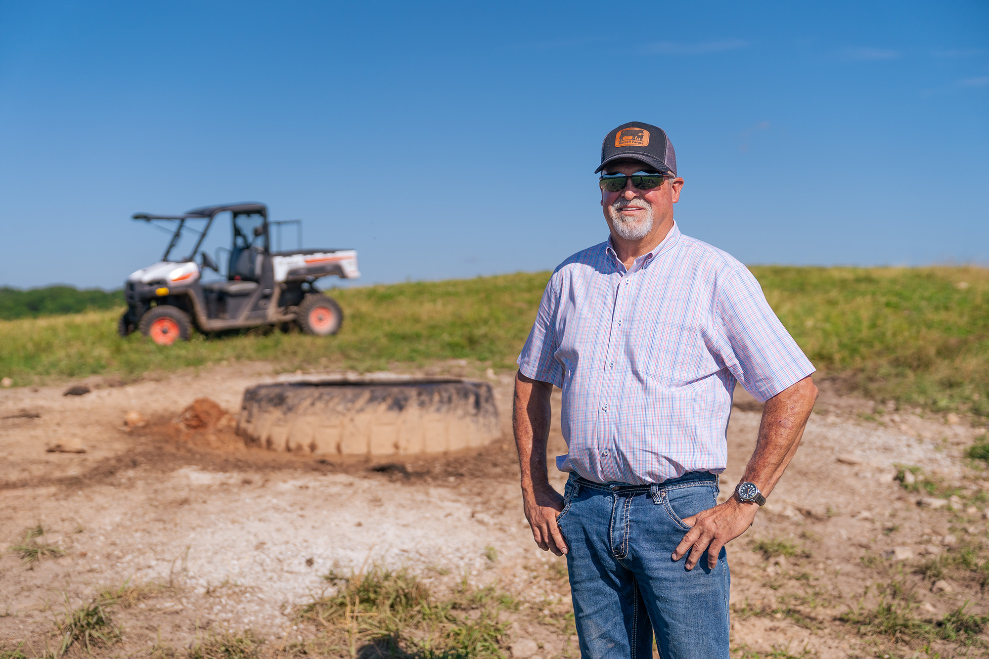 A man stands in a field smiling at the camera with a four-wheeler in the background.