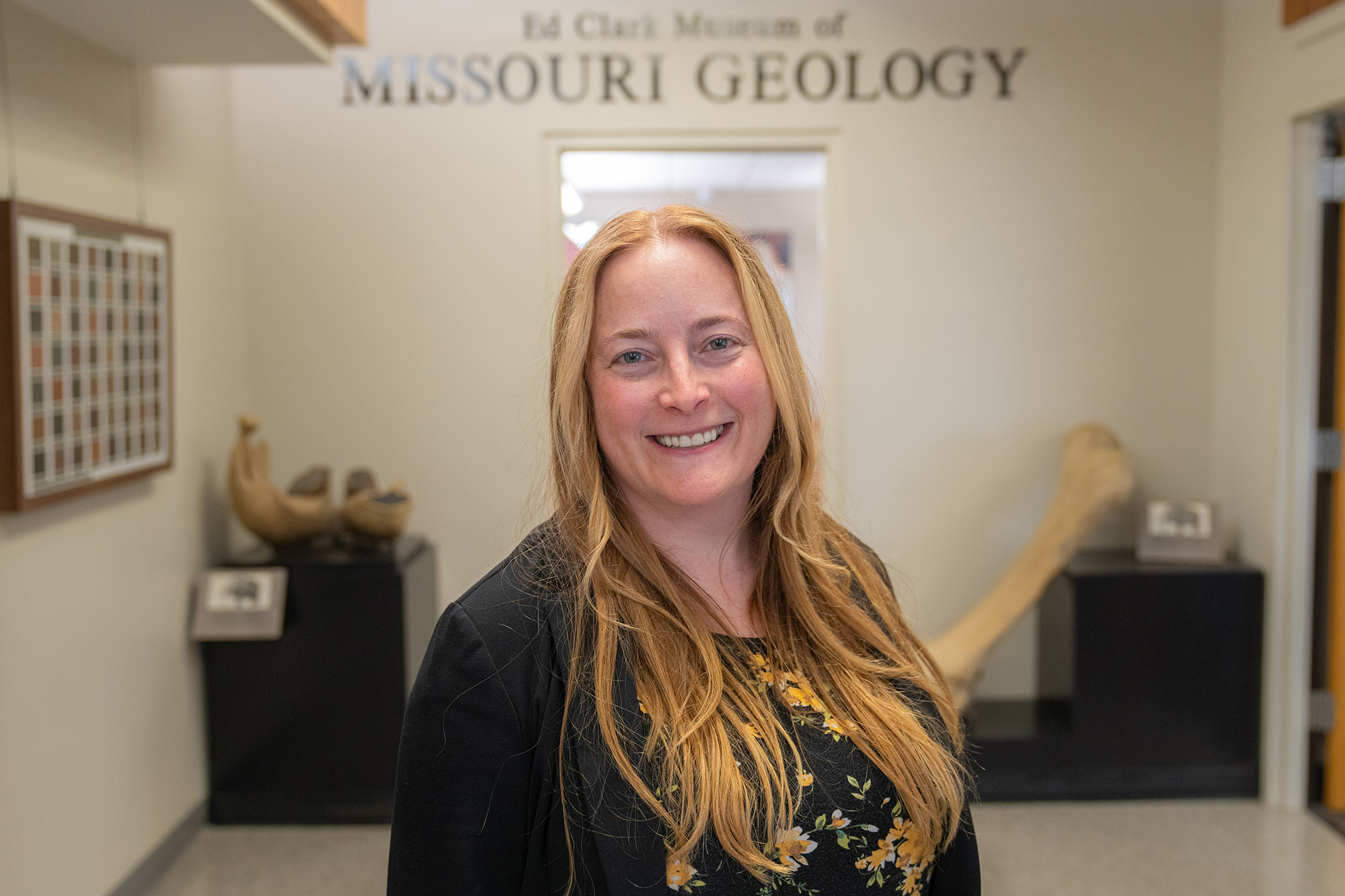 A woman stands smiling at the camera in front of the entrance to the Ed Clark Museum of Missouri Geology.