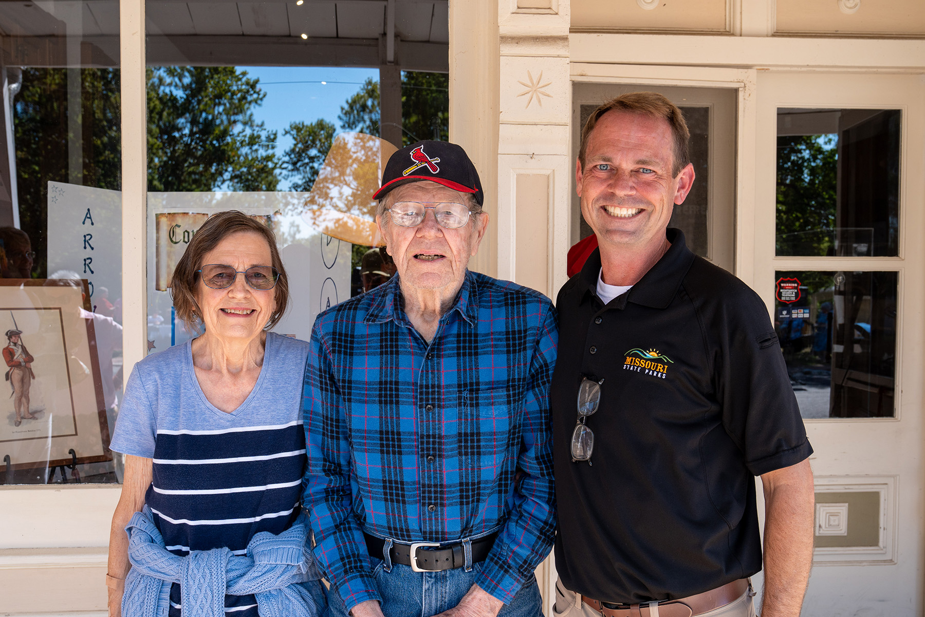 A man in a Missouri State Parks uniform stands next to an elderly man and woman. The elderly people are the parents of the uniformed man.