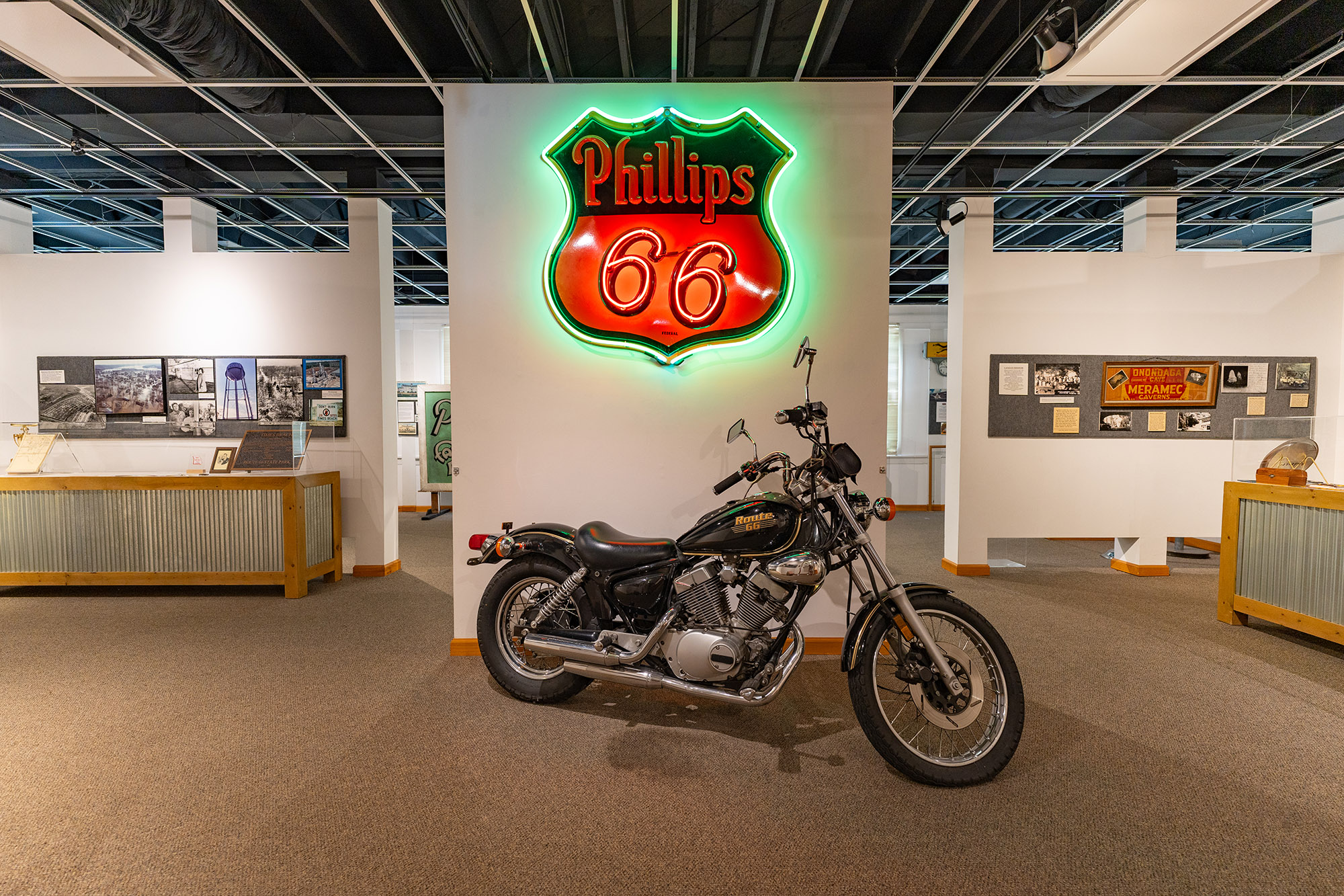 A classic motorcycle is displayed below a Phillips 66 neon sign, surrounded by other museum displays.