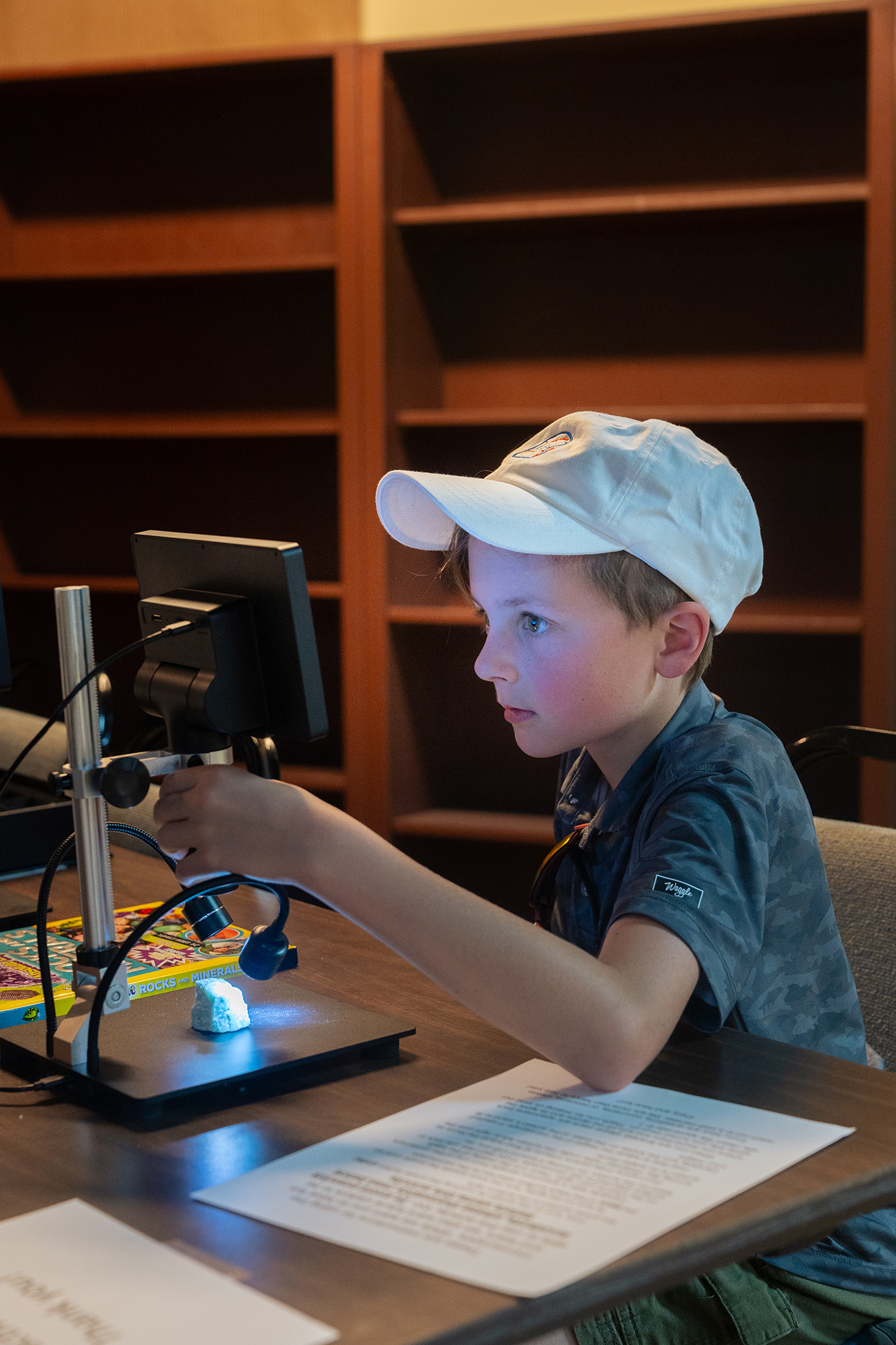 A young child sits close to a screen displaying a microscopic view of a brightly lit rock.