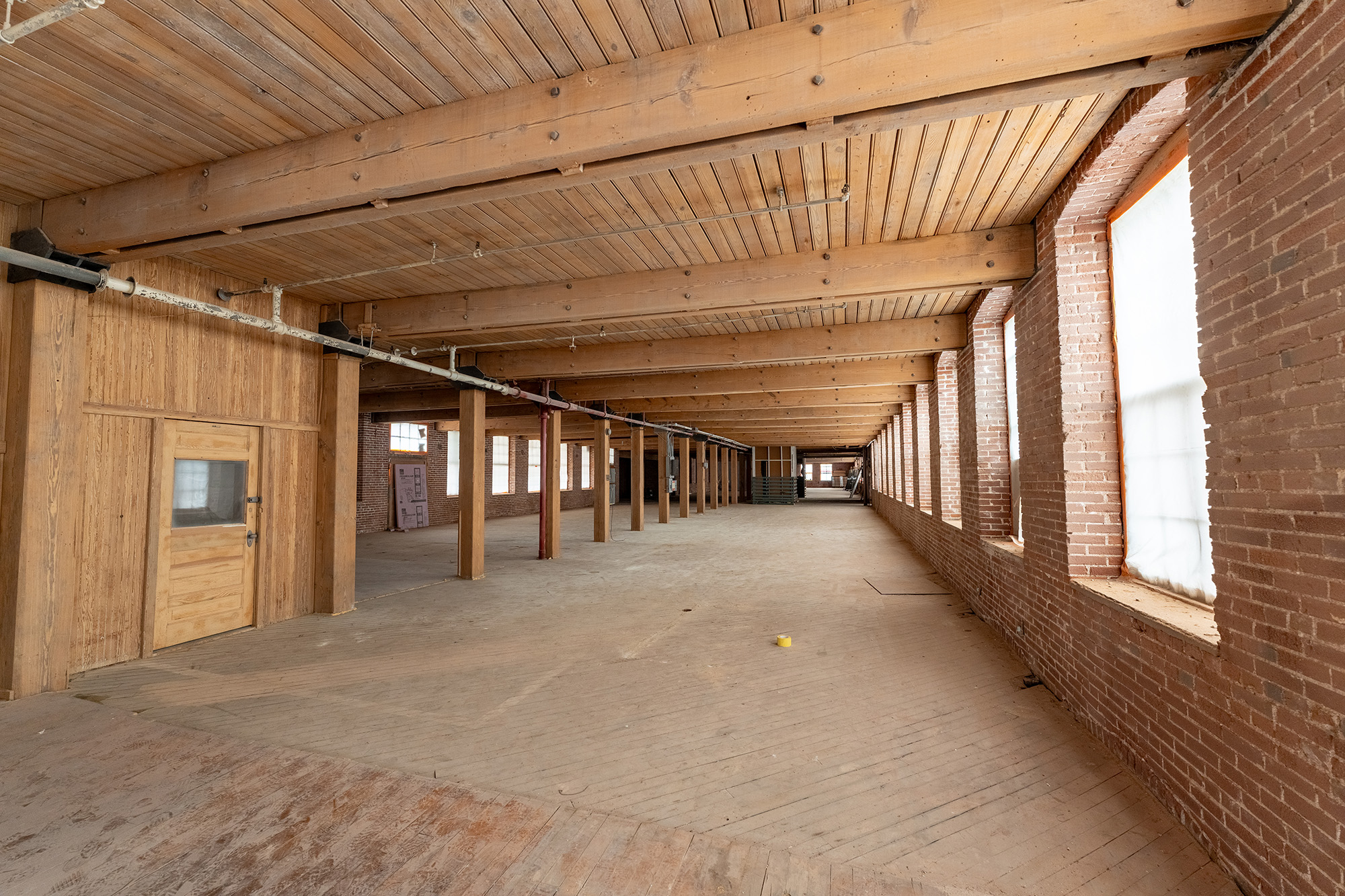 Interior of a partially renovated large room, wood floors, ceiling and pillars are the main features of the room.